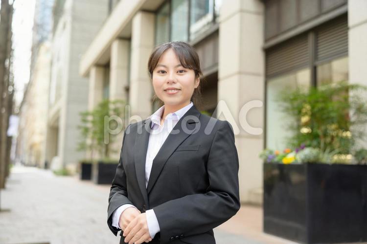ビル街でカメラ目線のスーツの女性 日本人,女性,20代の写真素材