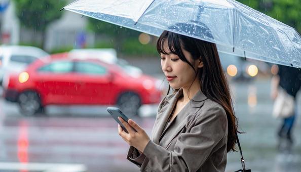 傘をさしてスマホを使う若い日本人女性 傘をさしてスマホを使う若い日本人女性の写真