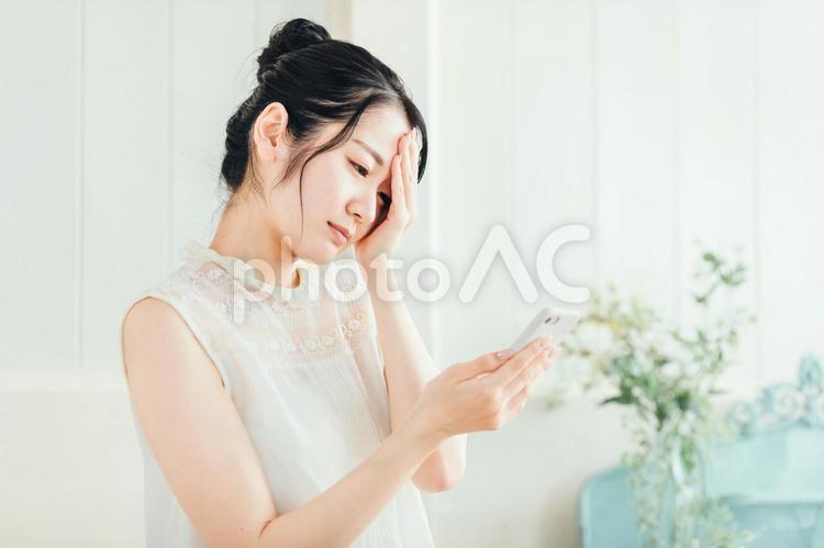 スマホを見て悩む女性（体調不良） 頭痛,スマホ,オンライン診療の写真素材