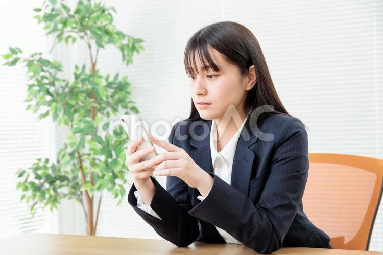 オフィスでスマホを動かす女性社員4 スーツ,企業,テーブルの写真素材