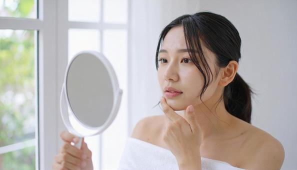 手鏡で顔を見てお肌の悩みに悩む若い女性 手鏡で顔を見てお肌の悩みに悩む若い女性の写真