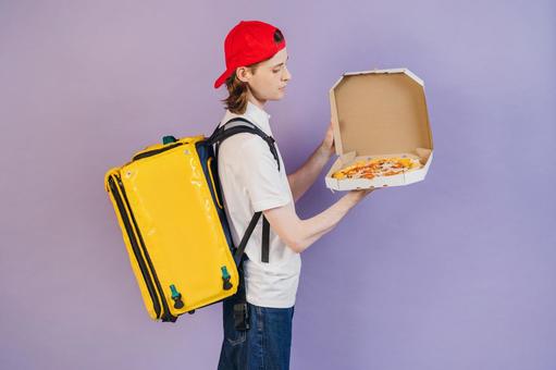 ピザ箱を開けて見せるフードデリバリーの男性（紫背景）の写真