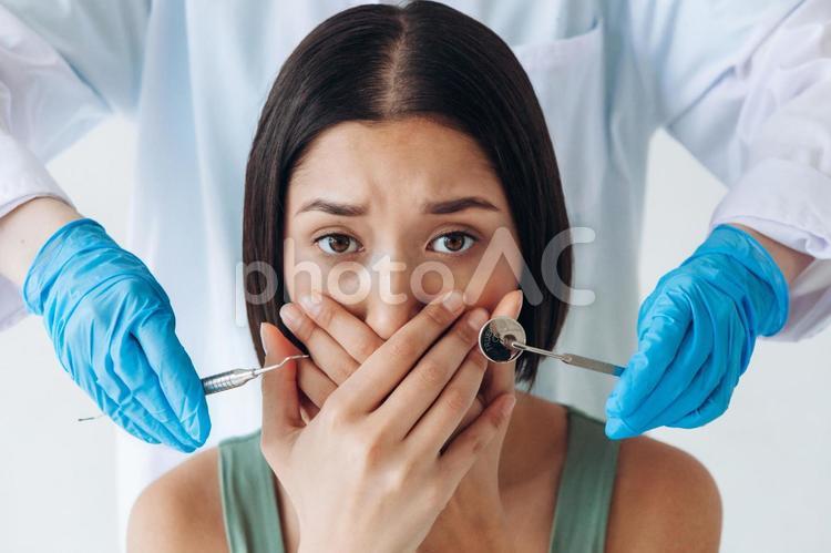 口元をおさえる女性と手袋の歯科医の手元 手元,女性,鏡の写真素材