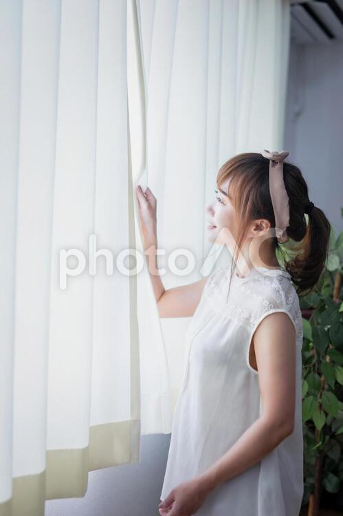白いカーテンから差し込む朝日を浴びる若い女性 横顔,女性,窓の写真素材