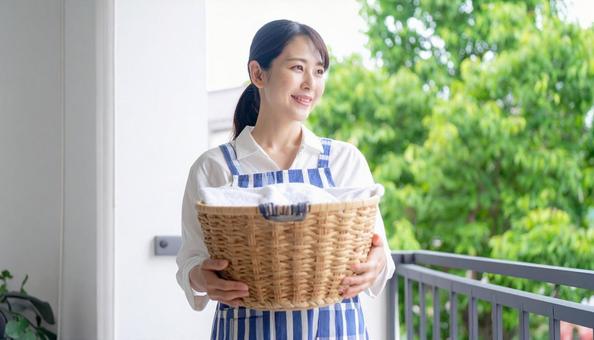 洗濯物が入った籠を抱えるエプロンの女性 洗濯物が入った籠を抱えるエプロンの女性の写真