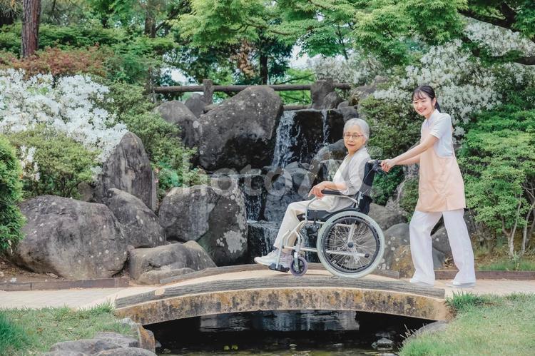 公園を散歩する高齢者女性と女性スタッフ（橋） 介護士,高齢者,看護師の写真素材