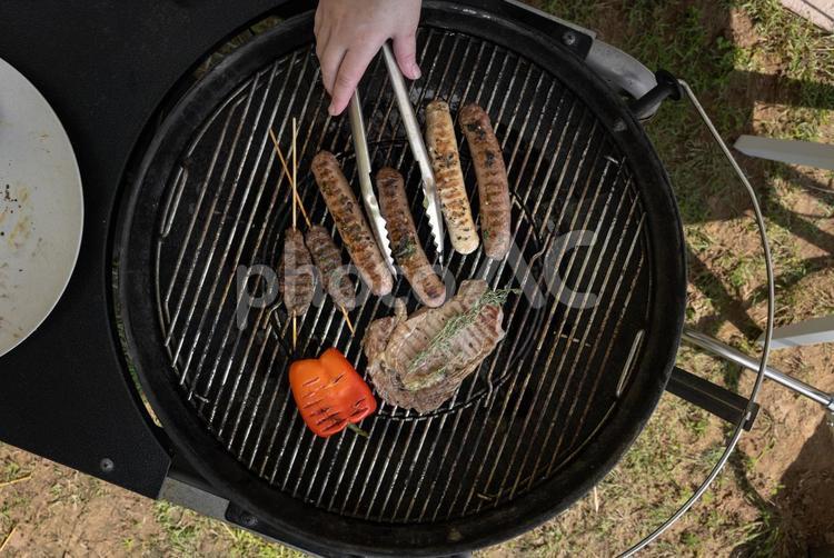 パプリカとステーキとソーセージなどをトングでつかむ人の手元 手元,人物,バーベキューの写真素材