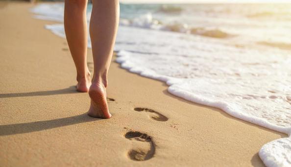 波打ち際の砂浜に足あとと女性の白い足 波打ち際の砂浜に足あとと女性の白い足の写真
