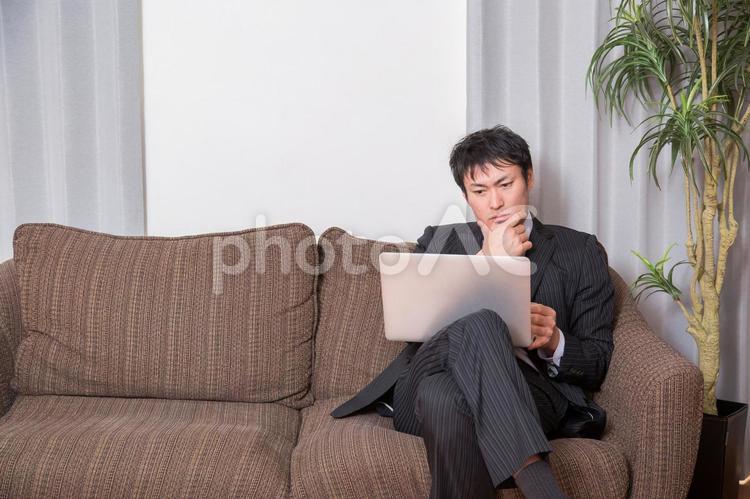 ソファでPCを開く男性 ノートパソコン,考える,男性の写真素材