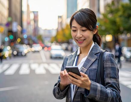 オフィス街でスマホを操作する女性社員 オフィス街でスマホを操作する女性社員の写真