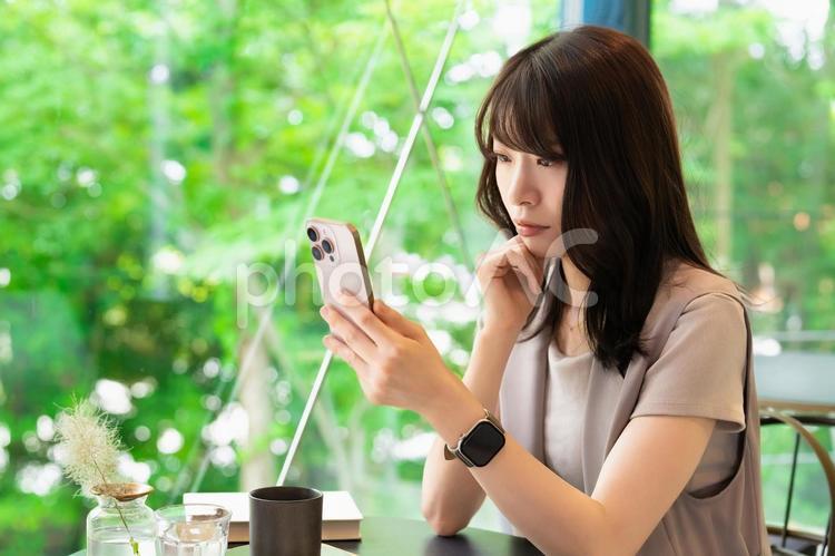 カフェでスマホを見ながら考える女性 女性,スマホ,スマートフォンの写真素材