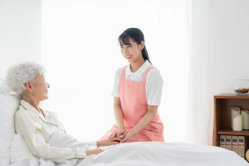 寝ているシニア女性を介護をする介護士 寝ているシニア女性を介護をする介護士の写真