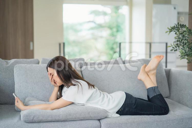 ソファで寝転んでスマホを使う女性（考える） スマホ,女性,ショックの写真素材