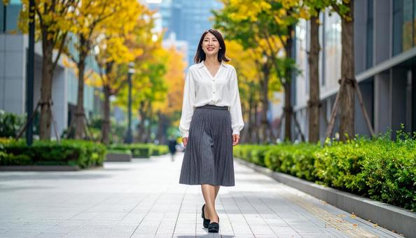秋のオフィス街を歩く笑顔の女性の写真