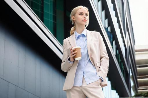 オフィスビルの外でコーヒーを持って立っている女性 ビジネスウーマン,ビジネス,女性の写真素材