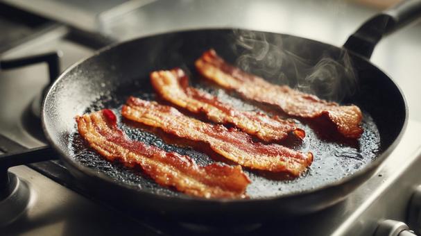 鉄のフライパンで焼かれるベーコン 鉄のフライパンで焼かれるベーコンの写真