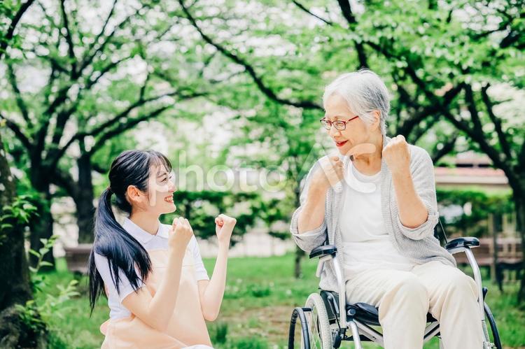 車椅子に乗った高齢者女性と女性スタッフ（ガッツポーズ） 介護士,高齢者,看護師の写真素材