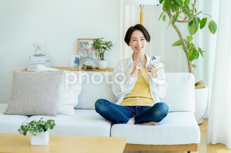 部屋でスマホを使うミドル女性 スマホ,笑顔,女性の写真素材