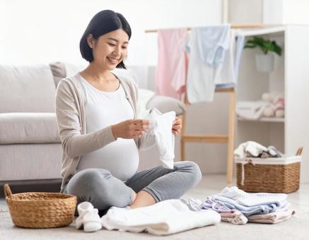ベビー服を畳みながら微笑む妊婦の準備時間の写真
