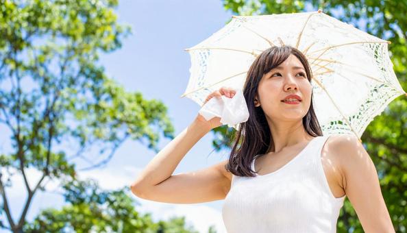 日傘をさして白いハンカチで汗を拭く女性 日傘をさして白いハンカチで汗を拭く女性の写真