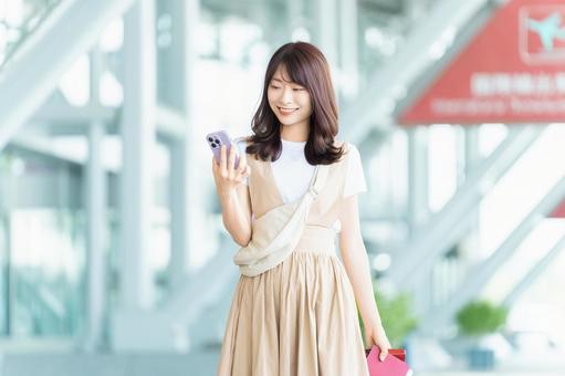 空港でスマホを使う旅行中の女性 空港でスマホを使う旅行中の女性の写真