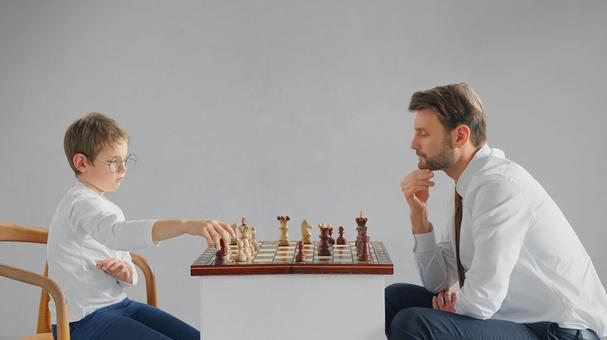 向かい合いチェスをするお父さんと男の子(グレー背景) 向かい合いチェスをするお父さんと男の子(グレー背景) チェス,親子,お父さんの写真素材
