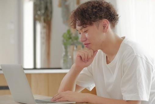リビングでパソコン作業をする若い男性 リビングでパソコン作業をする若い男性 考える,悩む,真剣の写真素材
