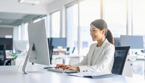 パソコンで仕事する白い服装の女性会社員 パソコンで仕事する白い服装の女性会社員の写真