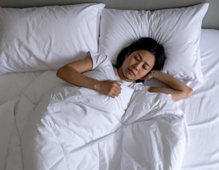 ベッドで寝苦しい女性 ベッドで寝苦しい女性の写真