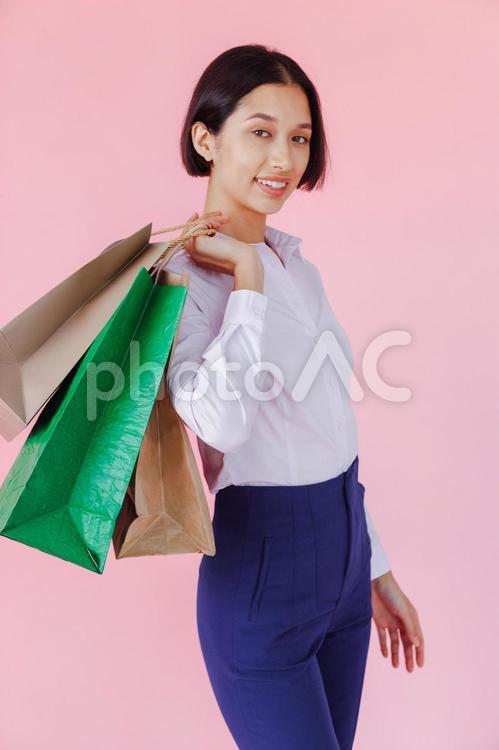 セールで買った物が入ったたくさんの紙袋を肩にかけて持っている女性（ピンク背景） セール,ショップ,女性の写真素材