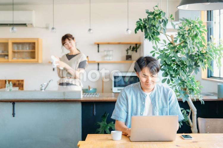 テレワークする男性とキッチンにいる女性（笑顔） テレワーク,パソコン,夫婦の写真素材