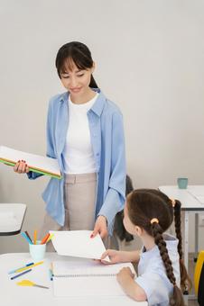 笑顔で女の子に何かを見せる先生 女性,女の子,子どもの写真素材