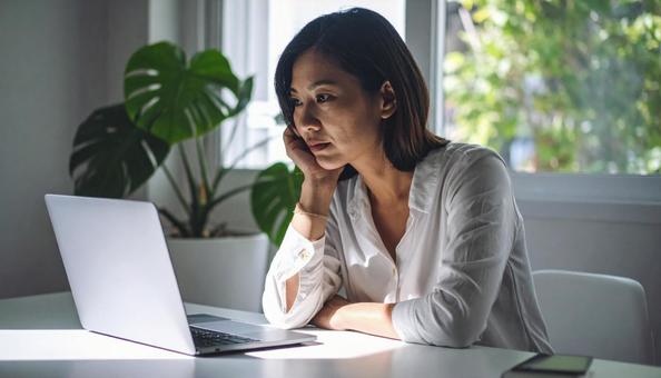 パソコンの前で悩む女性社員の写真