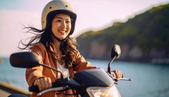 休日に海辺をバイクでツーリングする女性の写真