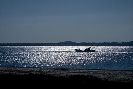 ＜素材＞夕暮れの光利輝く海を進む漁船の写真