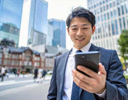 オフィス街でスマホを操作するビジネスマン オフィス街でスマホを操作するビジネスマンの写真