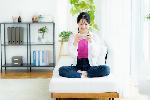 部屋でスマホを操作する若い女性 スマホ,笑顔,若い女性の写真素材