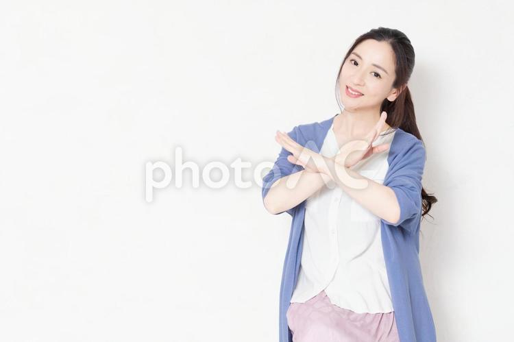 白い壁の前の椅子に座ってNGのポーズをする主婦 ng,駄目,女性の写真素材