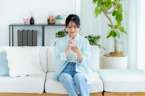 部屋でスマホを操作する若い女性 スマホ,笑顔,女性の写真素材