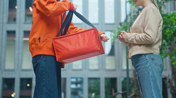 屋外でピザのデリバリーを受け取りにきた女性と配達員 配達,フードデリバリー,デリバリーの写真素材