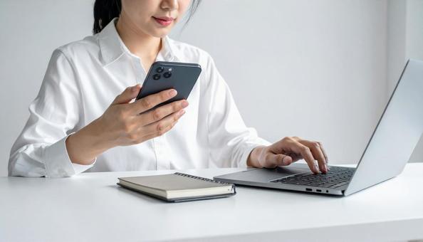 携帯を操作する女性の手元とノートパソコン 携帯を操作する女性の手元とノートパソコンの写真