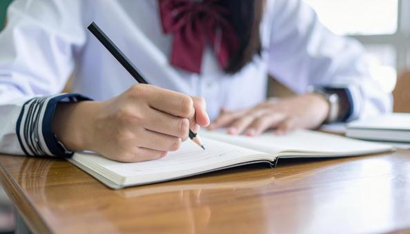 ノートに記入する日本人中学生の女の子の手の写真