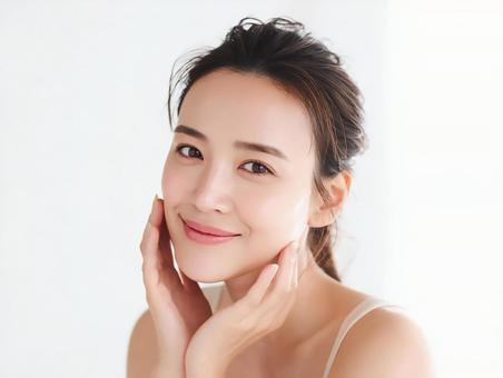 スキンケアして頬に触れる笑顔の女性の写真