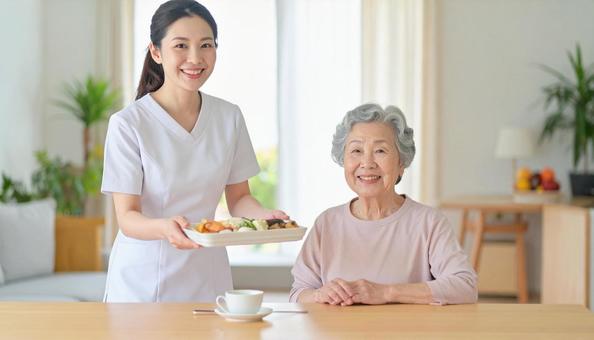 笑顔で食事を運ぶ女性介護士と高齢女性 笑顔で食事を運ぶ女性介護士と高齢女性の写真