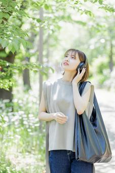 新緑の中ヘッドフォンで音楽を聴く若い女性 新緑の中ヘッドフォンで音楽を聴く若い女性 女性,外出,ヘッドフォンの写真素材