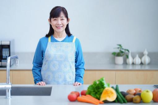 キッチンでエプロン姿の中年女性と色とりどりの野菜 キッチンでエプロン姿の中年女性と色とりどりの野菜の写真