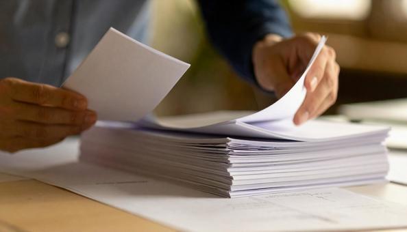 重なった白いコピー用紙をめくる手の写真