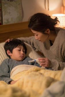 ベッドで辛そうな表情の男の子と母親 ベッドで辛そうな表情の男の子と母親の写真