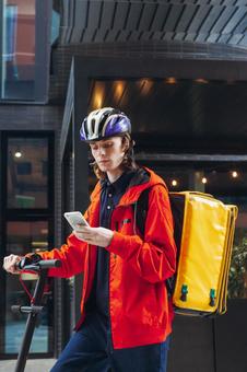 街なかでスマートフォンを見ているフードデリバリーの男性 配達,フードデリバリー,デリバリーの写真素材