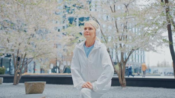 ヘッドフォンをしたシニア女性が足を伸ばして準備運動している様子 ヘッドフォンをしたシニア女性が足を伸ばして準備運動している様子の写真